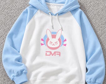 Op de afbeelding: Een wit en lichtblauw raglan-hoodie met een roze en witte konijngrafiek en de tekst D.VA eronder gedrukt. De trui met capuchon heeft een bijpassende lichtblauwe capuchon met witte trekkoorden en geribbelde boorden en zoom.