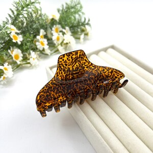 May include: A hair claw clip featuring a brown and black tortoiseshell pattern. The accessory has a curved top edge and multiple interlocking teeth along the bottom, designed to hold hair securely in place with a spring-loaded mechanism.