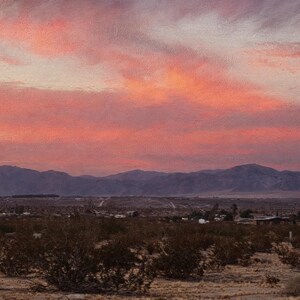 Puede incluir: Una pintura de paisaje de un desierto al atardecer con un cielo vibrante en tonos rosa y naranja sobre cadenas monta&ntilde;osas oscuras. El primer plano muestra arbustos des&eacute;rticos bajos y vegetaci&oacute;n dispersa en terreno arenoso.