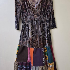May include: A long-sleeved dress featuring a dark brown velvet bodice with a v-neckline and an elasticized waist. The skirt is constructed from a patchwork of various fabrics in solid colors, including orange, purple, and teal, alongside patterned textiles.