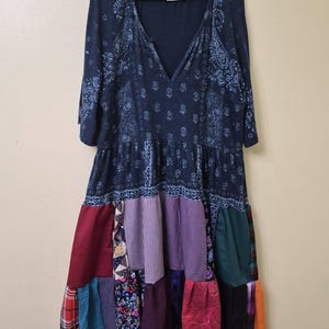 May include: A knee-length dress with a dark blue paisley print bodice and a V-neckline. The skirt features a patchwork design composed of various fabric panels in colors including maroon, purple, dark green, black, and plaid patterns.