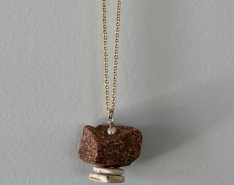 May include: A gold chain necklace with a brown and white geometric pendant.