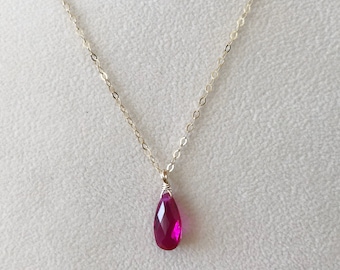 May include: A delicate gold chain necklace with a teardrop-shaped pendant featuring a vibrant pink gemstone.
