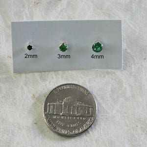 May include: Three green gemstone earrings on a white card with measurements in millimeters: 2mm, 3mm, and 4mm. A US quarter is shown for size comparison.