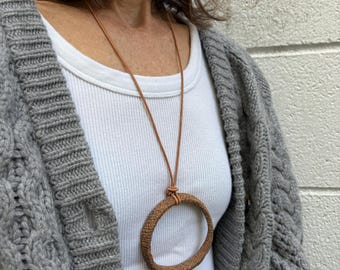 May include: A brown leather cord necklace with a large oval pendant made of woven natural material.