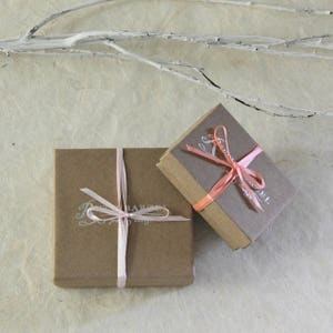 May include: Two small brown gift boxes with pink ribbon bows. The boxes are tied with ribbon and have a white label with the text "The Barefoot Gypsy Jewelry Shop" printed on them.