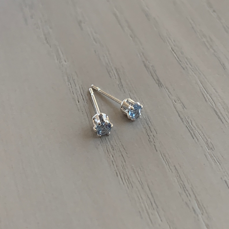 May include: A pair of silver stud earrings with small, clear gemstones.