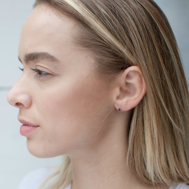 May include: A close-up of a person's ear with a small black stud earring. The earring is set in a silver or white gold setting.