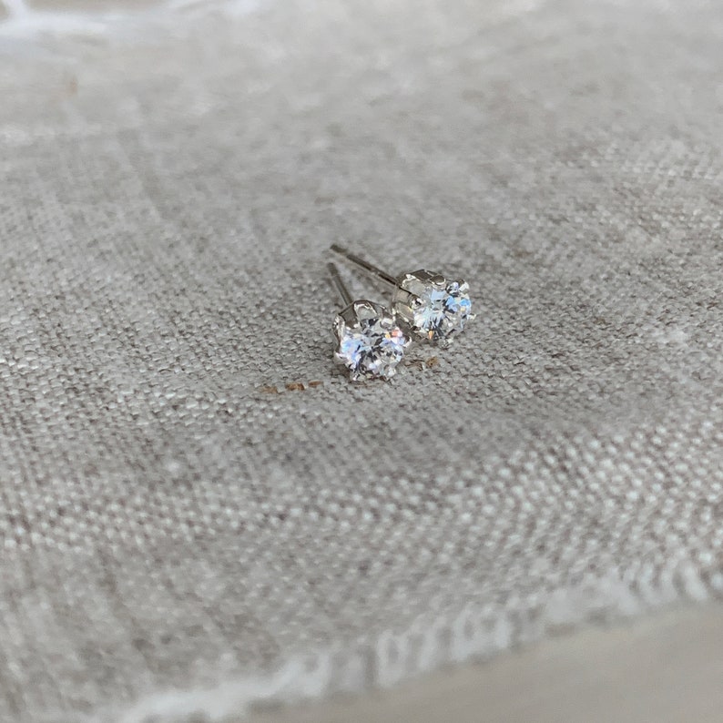 May include: A pair of silver stud earrings with clear round cubic zirconia stones.