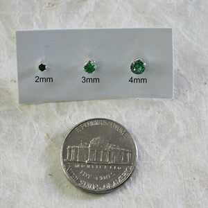 May include: Three green gemstone earrings on a white card with measurements in millimeters: 2mm, 3mm, and 4mm. A US quarter is shown for size comparison.