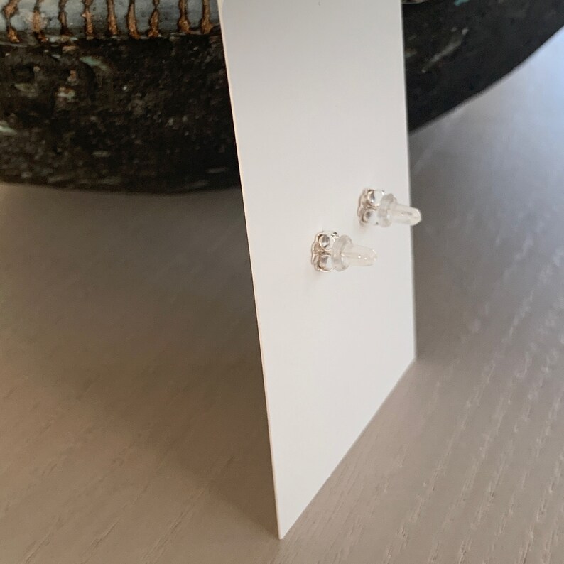 May include: A pair of silver stud earrings with clear stones on a white background.