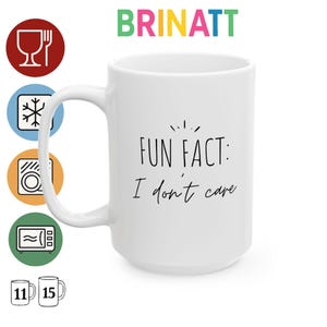 Puede incluir: Una taza de cerámica blanca con el texto negro Fun Fact: I don't care. A la izquierda hay cinco iconos circulares que representan seguridad alimentaria, congelador, lavavajillas y microondas, junto a indicadores de 11 y 15 onzas.