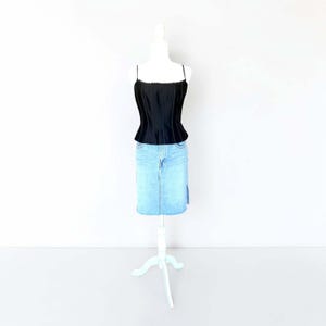 May include: A black corset-style top with thin spaghetti straps and a scalloped neckline edge, paired with a light blue denim skirt featuring a central vertical seam and a side slit, displayed on a white mannequin torso.