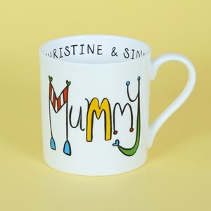 May include: White ceramic mug with a black outline of the word "Mummy" in yellow, red, blue, and green. The top rim of the mug has the text "Kristine & Sid" in black.