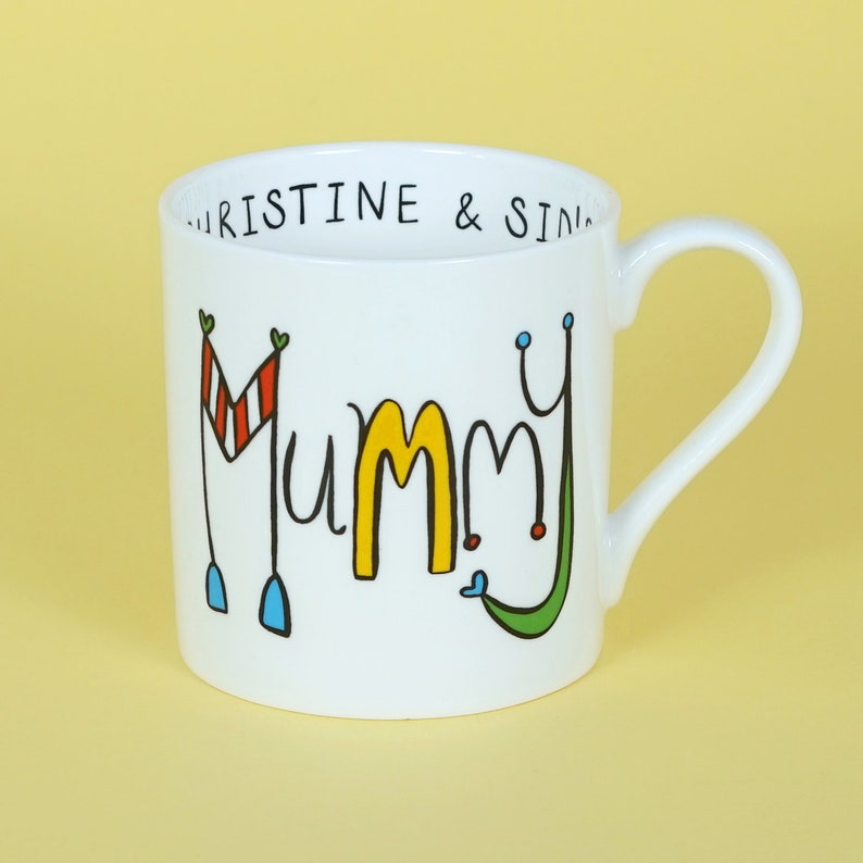 May include: White ceramic mug with a black outline of the word "Mummy" in yellow, red, blue, and green. The top rim of the mug has the text "Kristine & Sid" in black.