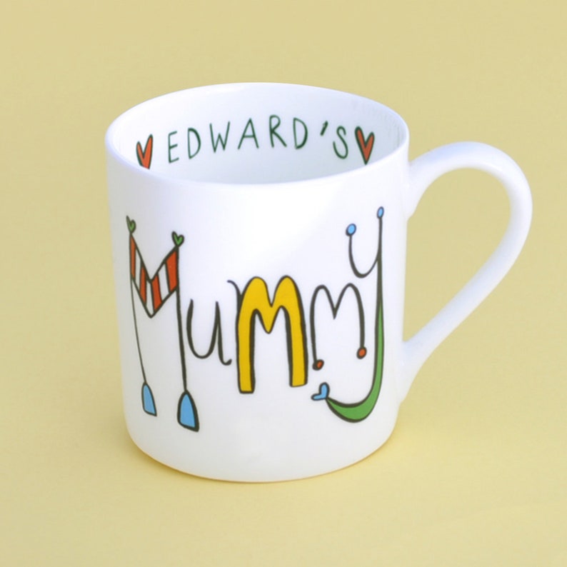 May include: White ceramic mug with a colorful design that says "Mummy" and "Edward's" in green lettering. The mug has a handle.