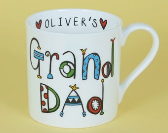 May include: White ceramic mug with a colorful design that says "Grand Dad" and "Oliver's" in a heart.