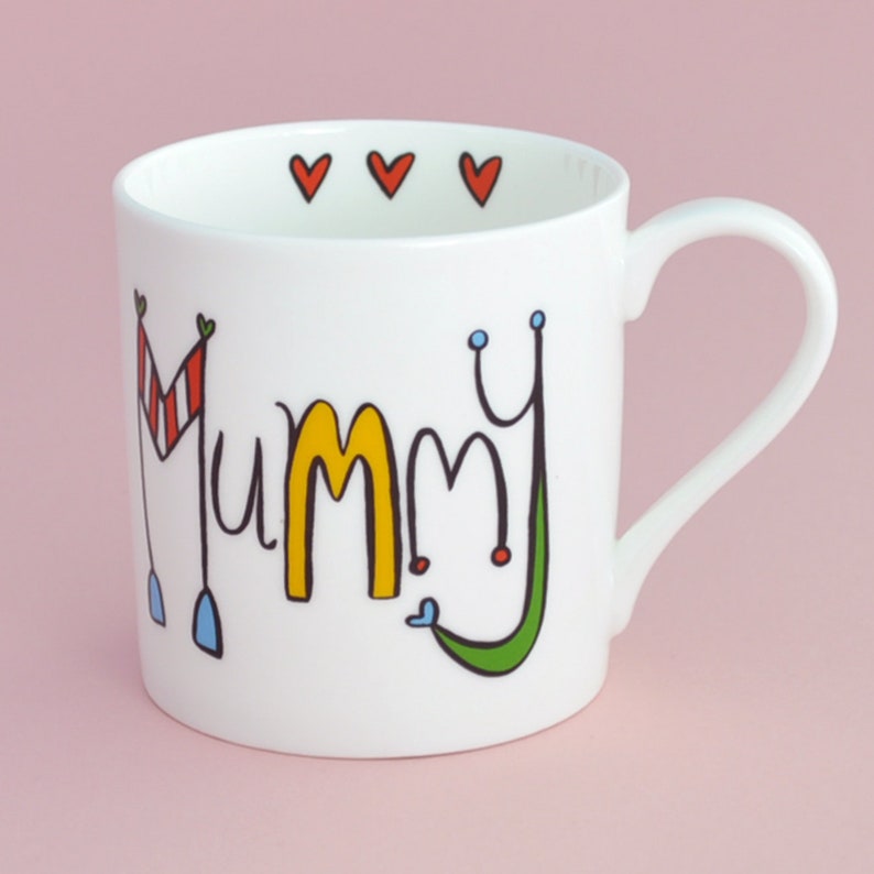 May include: White ceramic mug with a colorful design that says "Mummy" with hearts around the rim.