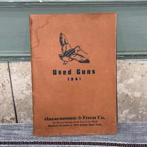 May include: A tan vintage booklet titled Used Guns 1941 with a black illustration of a bird in flight. The cover features the text Abercrombie & Fitch Co. The Greatest Sporting Goods Store in the World, Madison Avenue at 45th Street, New York.