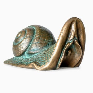 Könnte beinhalten: Eine bronzefarbene Metallskulptur in Form einer Schnecke mit detailliertem Spiralgehäuse und strukturiertem Körper. Die Oberfläche zeigt eine verwitterte Patina mit dunkelbraunen und oxidgrünen Akzenten, die komplexe Muster auf Gehäuse und Haut betonen.