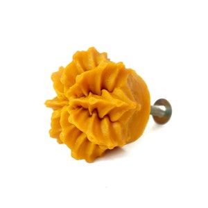 May include: A yellow ceramic cabinet knob with a decorative, ruffled design. The knob has a metal screw for attaching to a cabinet door.