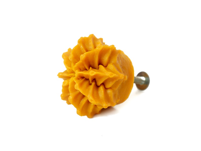 May include: A yellow ceramic cabinet knob with a decorative, ruffled design. The knob has a metal screw for attaching to a cabinet door.