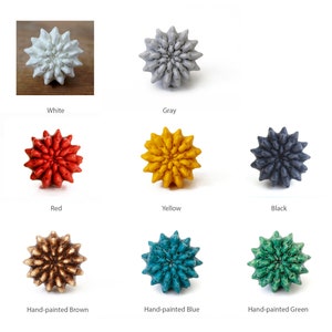 May include: Nine ceramic knobs in various colors, including white, gray, red, yellow, black, brown, blue, and green. The knobs are shaped like a stylized flower with multiple points.