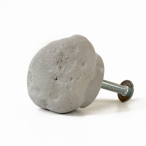 May include: A gray concrete knob with a rough texture and a silver metal screw. The knob is designed to resemble a rock.