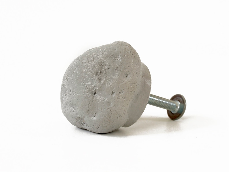 May include: A gray concrete knob with a rough texture and a silver metal screw. The knob is designed to resemble a rock.