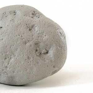 May include: A single, smooth, gray stone with a slightly irregular shape. The stone has a rough, textured surface.