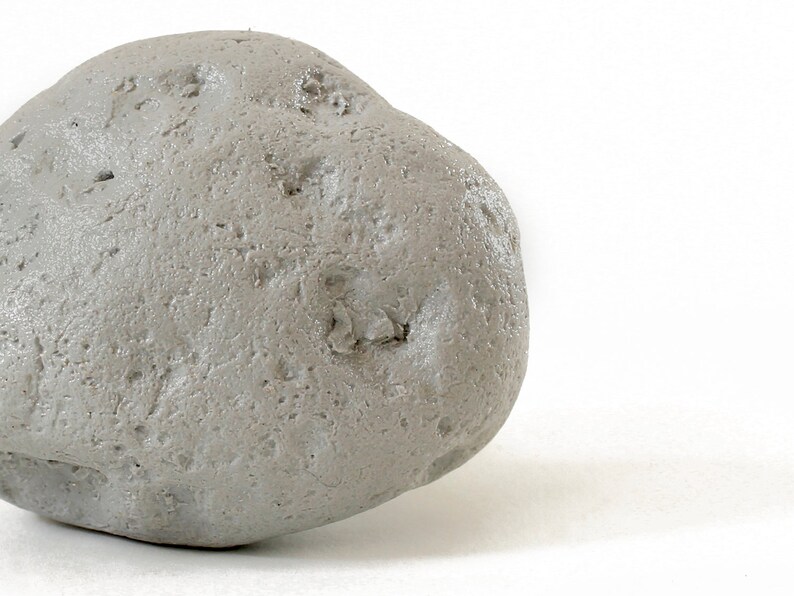 May include: A single, smooth, gray stone with a slightly irregular shape. The stone has a rough, textured surface.