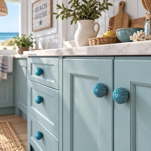 May include: Light blue kitchen cabinetry featuring round, textured sea urchin-shaped knobs in a matching blue hue. The cabinet doors and drawers have a classic recessed panel design, providing a clean and structured look to the kitchen storage units.