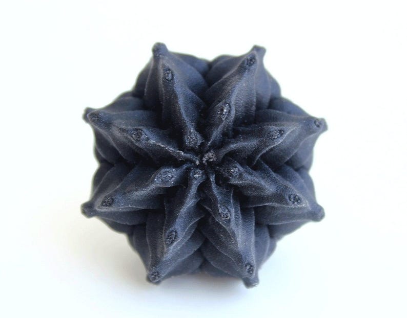 May include: A dark navy blue, multi-pointed star-shaped object with a complex, folded geometric structure. The surface features numerous sharp, symmetrical peaks radiating from the center, creating a dense, layered, and textured appearance.