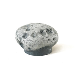 May include: A small, gray, rocky asteroid with a rough, cratered surface. The asteroid is made of a lightweight material and is painted in a realistic, weathered style.