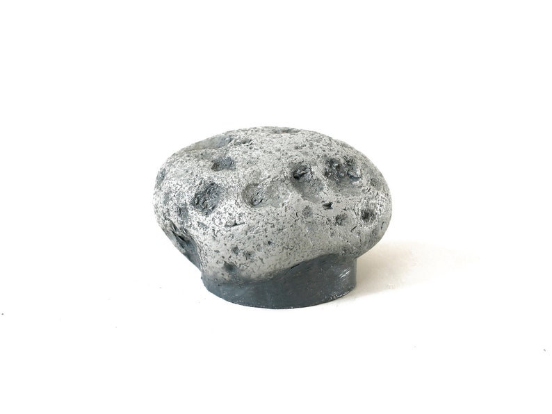 May include: A small, gray, rocky asteroid with a rough, cratered surface. The asteroid is made of a lightweight material and is painted in a realistic, weathered style.