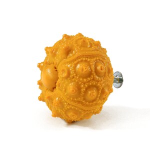 Puede incluir: Un pomo de armario en forma de erizo de mar amarillo con un tornillo plateado.