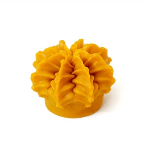 Op de afbeelding: Een gele, bloemvormige kaars met een getextureerd oppervlak.