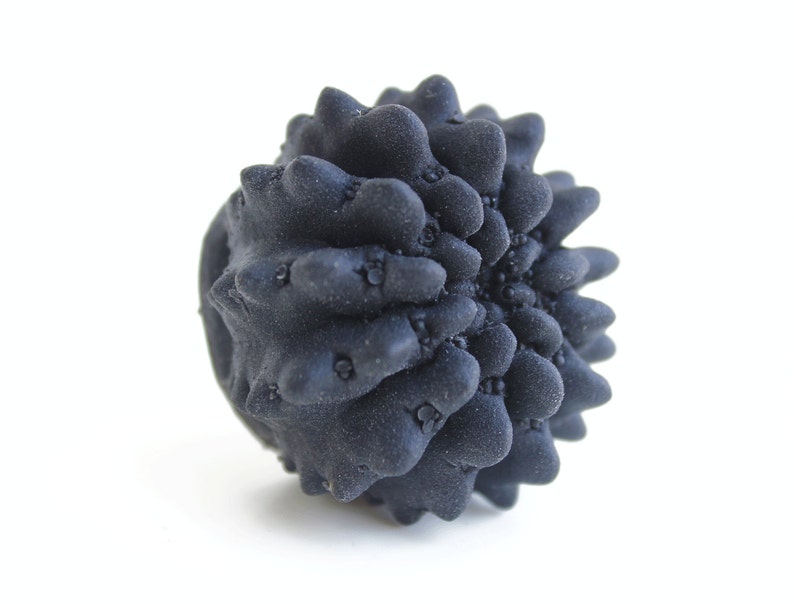May include: A black, spiky, round object resembling a sea urchin. The object is made of a textured material and has a rough surface.