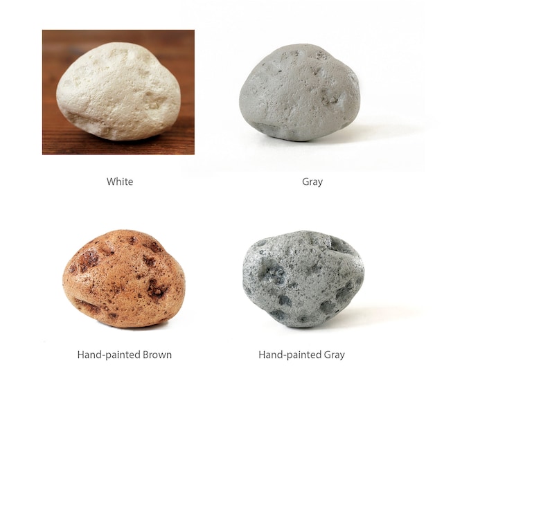 May include: Four smooth, round stones in different colors: white, gray, brown, and hand-painted gray. The stones are all about the same size and shape.
