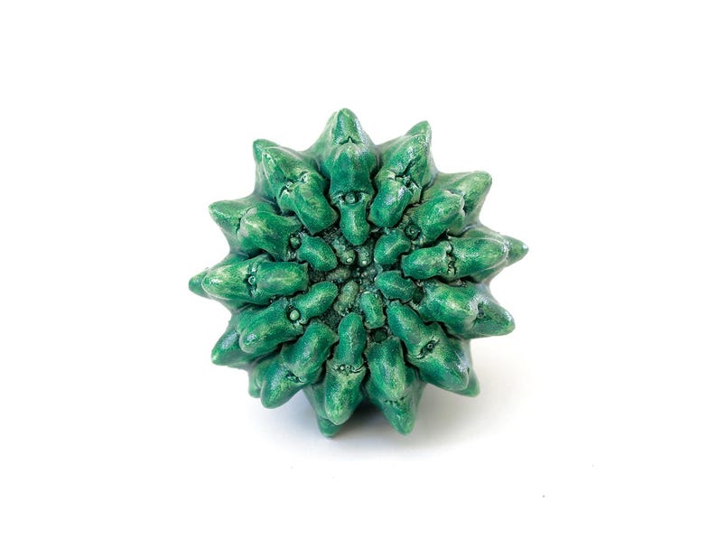 May include: A circular ceramic object with a vibrant green glaze, featuring a radial pattern of numerous pointed, thorn-like protrusions that extend outward from a dense, textured center, creating a complex, multi-faceted, star-like appearance.