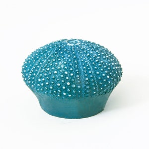 May include: A teal blue sea urchin shaped ceramic ornament with white dots.