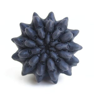 May include: A dark charcoal gray, star-shaped object with a textured, matte surface. The item features numerous rounded, protruding points radiating from a central core, creating a dense, multi-layered, and symmetrical floral-like structure.
