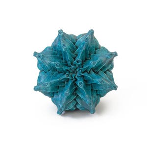 May include: A teal-colored, multi-faceted geometric object with a star-like, symmetrical structure. The surface features a textured, matte finish with deep blue and green tones, composed of numerous pointed, triangular segments radiating outward.