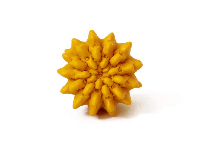 May include: A bright yellow, spherical object with a textured, multi-pointed surface resembling a stylized sun or a geometric flower. The form features numerous protruding, tapered segments radiating from a central point, creating a dense, uniform pattern across the entire exterior of the round item.