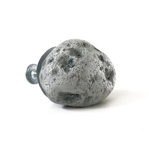 May include: A gray stone-shaped cabinet knob with a textured surface. The knob is attached to a silver screw.