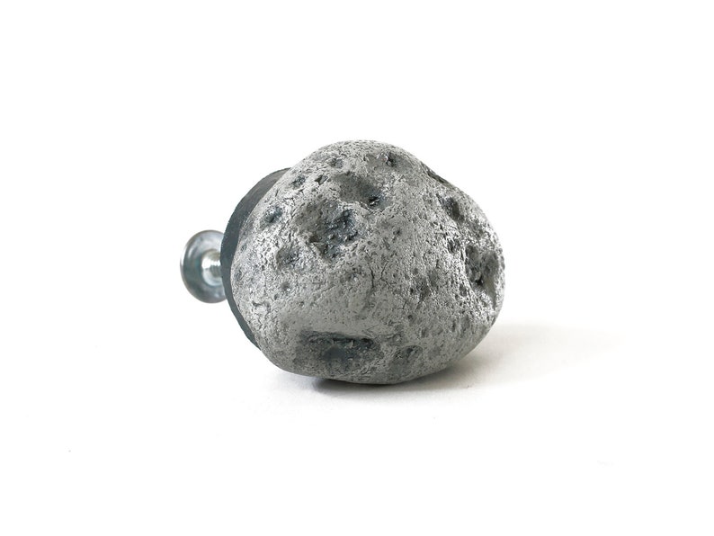 May include: A gray stone-shaped cabinet knob with a textured surface. The knob is attached to a silver screw.