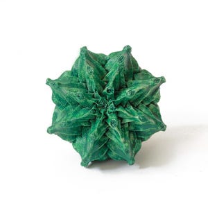 May include: A geometric, star-shaped object in a deep forest green color. The item features a complex, multi-layered structure with numerous pointed, triangular protrusions radiating from the center, creating a dense, textured, and symmetrical form.