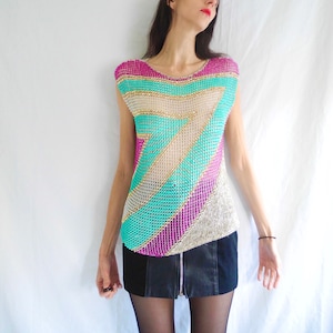May include: A sleeveless top made of silver, pink, and turquoise chainmail. The top has a geometric pattern and is worn over a black skirt.