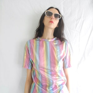 May include: A woman wearing a short-sleeved iridescent rainbow striped shirt with a black skirt and white cat-eye sunglasses.