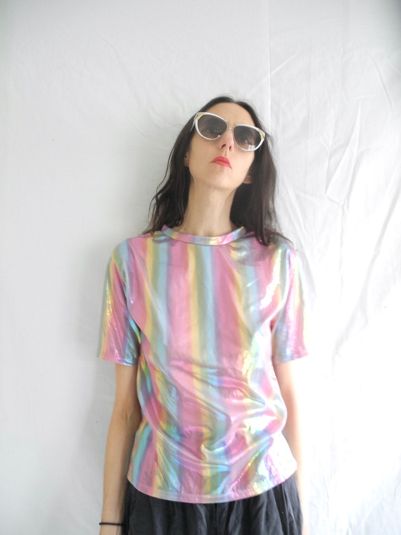 May include: A woman wearing a short-sleeved iridescent rainbow striped shirt with a black skirt and white cat-eye sunglasses.